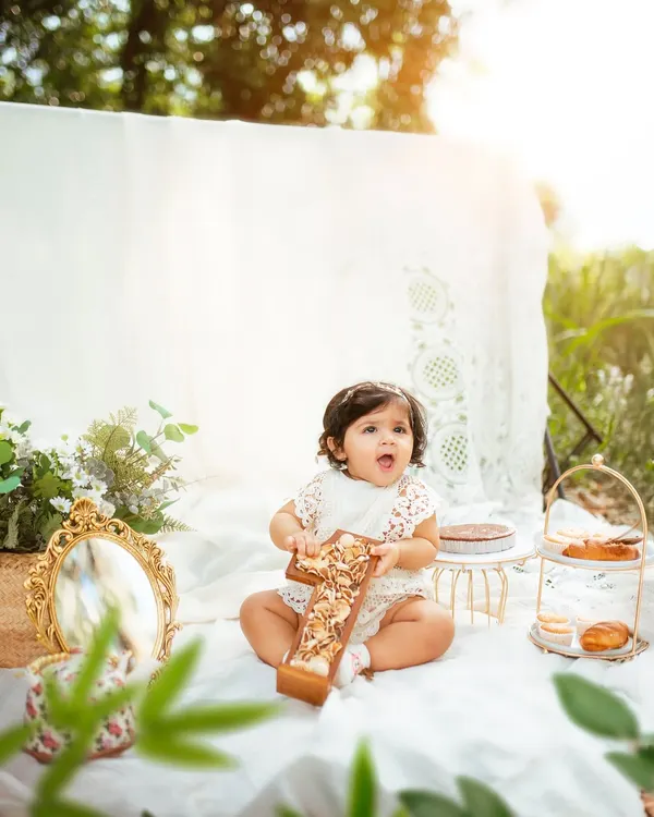 A perfect first birthday picnic. This little girl is holding a wooden "One" prop, surrounded by beautiful decor in the warm afternoon sun.
