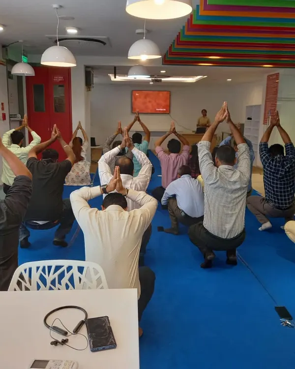 A team practices a simple standing asana during an office wellness workshop. These sessions are designed to be done in work clothes, making it easy to integrate a moment of wellbeing into a busy corporate schedule.