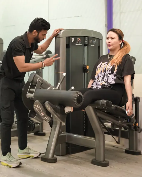 My approach to personal training is hands-on. Here, I am guiding a client through a leg extension, ensuring her form is perfect to maximize results and prevent injury.