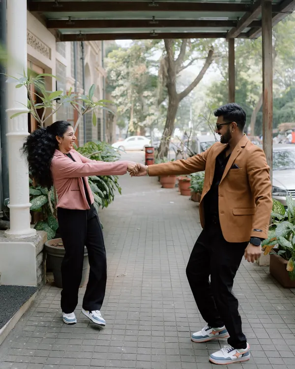 A fun, candid shot of a couple in modern blazers, dancing and laughing on a city sidewalk. This photo captures the playful energy of an urban pre-wedding shoot in Mumbai.