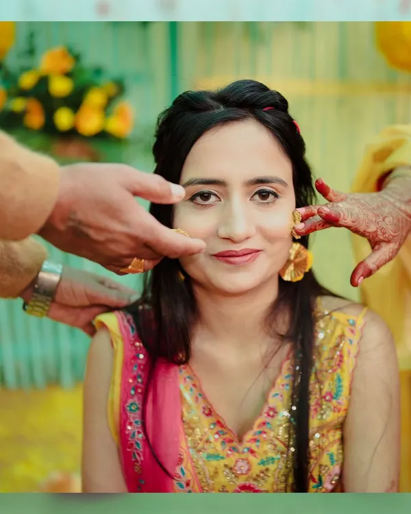 A classic Haldi portrait. We capture the moment the turmeric paste is first applied, focusing on the bride's calm expression and the hands of loved ones blessing her.