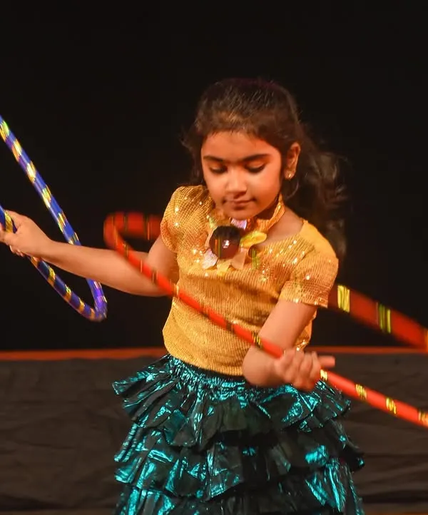 A close-up of one of our young performers skillfully maneuvering multiple hoops during a stage performance. It's a testament to the coordination and focus they build in our classes.