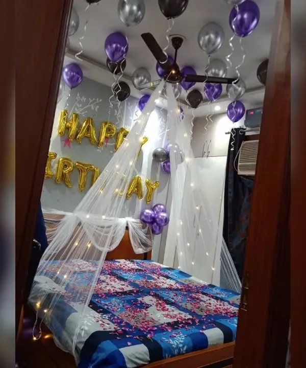 A classic birthday surprise featuring a canopy with fairy lights over the bed, and purple and silver balloons on the ceiling and floor.