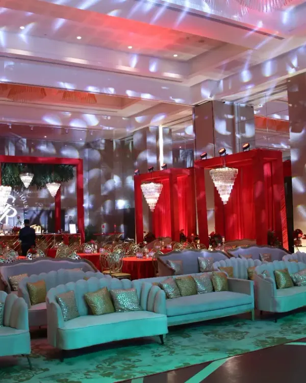 A wide view of a luxurious sangeet hall, decorated in a bold red and gold theme. We arranged elegant lounge seating to create a comfortable yet glamorous atmosphere for guests.