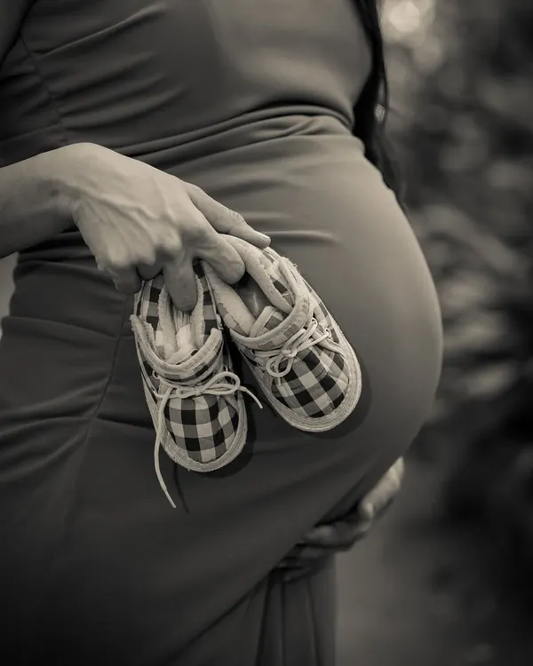 A close-up, artistic shot focusing on the tiny details. These little plaid shoes, held against the bump, tell a big story in classic black and white.