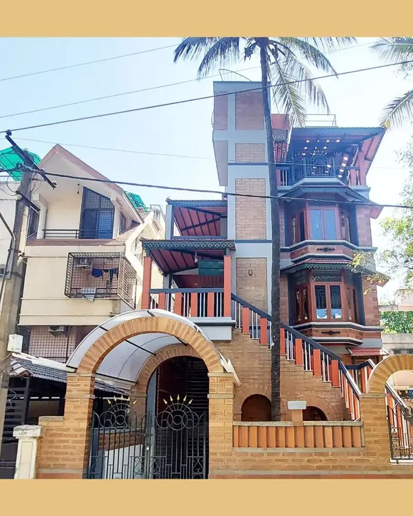 The full facade of the Basavanagudi residence, showcasing a dynamic interplay of materials, from the arched brick entrance to the intricate bay windows and shaded balconies.
