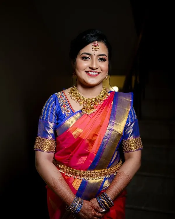 A radiant smile for an engagement ceremony. This classic South Indian look features a flawless base, defined eyes, and a joyful red lip, perfectly complementing the vibrant silk saree and traditional temple jewellery.