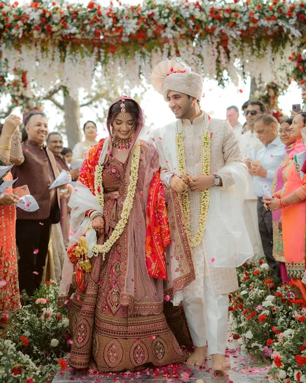 The couple walks together after their jaimala ceremony, surrounded by smiling family and a shower of petals. This captures the joy of a Hindu wedding.