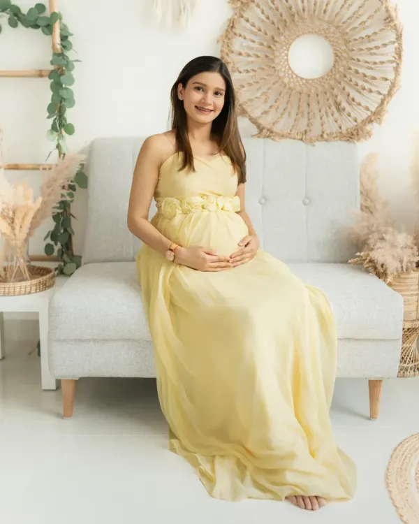 Seated comfortably in my bright, boho-chic studio, this mother-to-be radiates serenity in a soft yellow gown. The natural textures of the decor create a warm and inviting atmosphere.