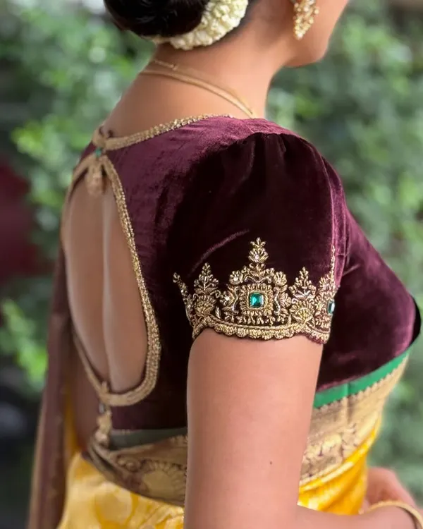 A client showcasing the elegant back cutout and puff sleeves of her deep wine velvet blouse. The gold zardosi embroidery on the sleeve cuff adds a touch of regal splendor.