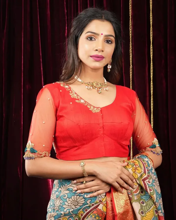This bright red blouse features sheer sleeves with delicate embroidery at the cuffs, adding a touch of elegance to a bold color.