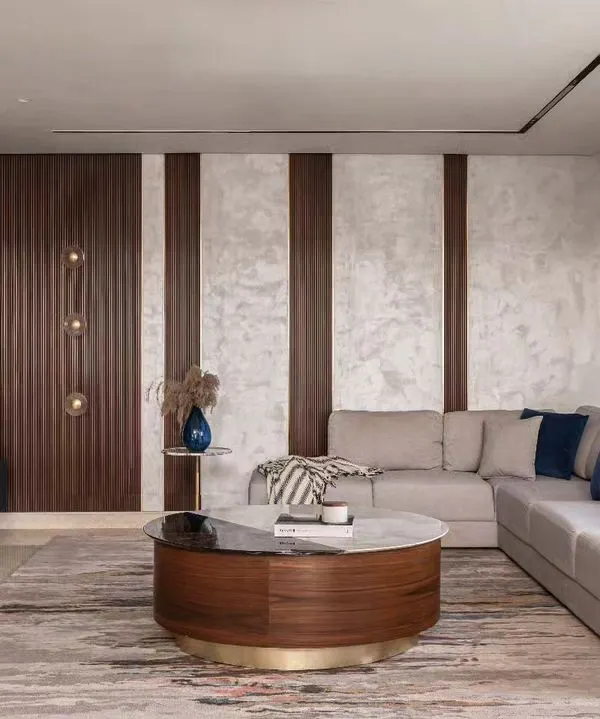 Getting the scale of furniture right is key to a room's flow. In this living room, the large L-shaped sofa defines the seating area without overwhelming it, while the round coffee table adds a contrasting shape and keeps movement easy. The mix of wood, marble, and textured wallpaper creates a layered, sophisticated look.