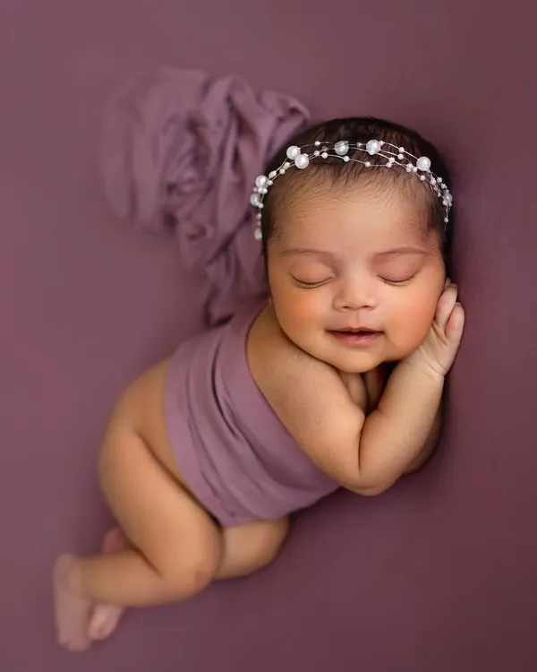 That tiny newborn smile is everything! I love capturing these fleeting moments. This little one is posed so peacefully on a simple purple backdrop, making her the star of the show.