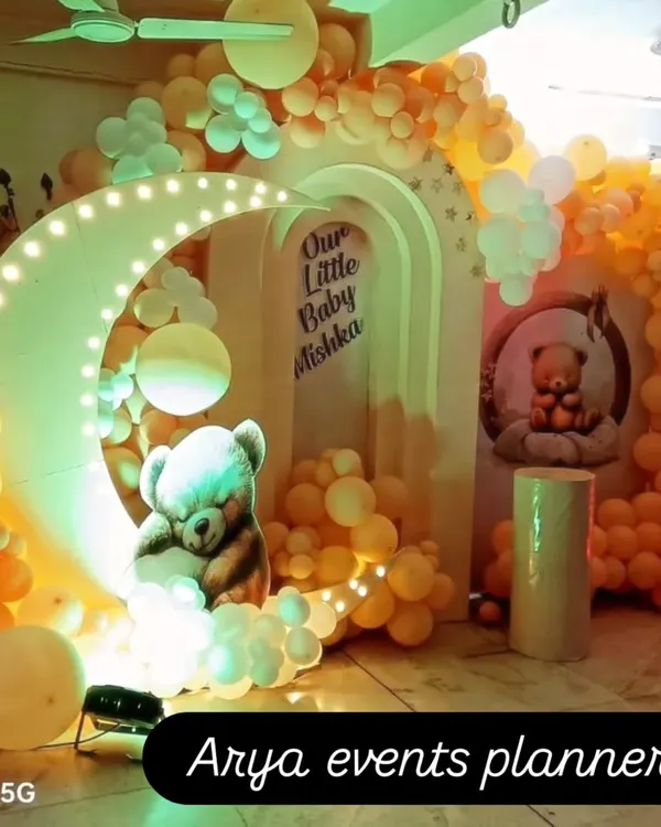A dreamy naming ceremony decoration featuring a light-up crescent moon, a sleeping teddy bear prop, and a warm-toned balloon arch for "Our Little Baby Mishka".