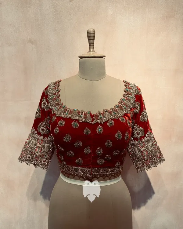 A royal red velvet blouse for bride Bhavana, featuring a neckline designed to resemble jewelry, embellished with kundan, pearls, and beads.