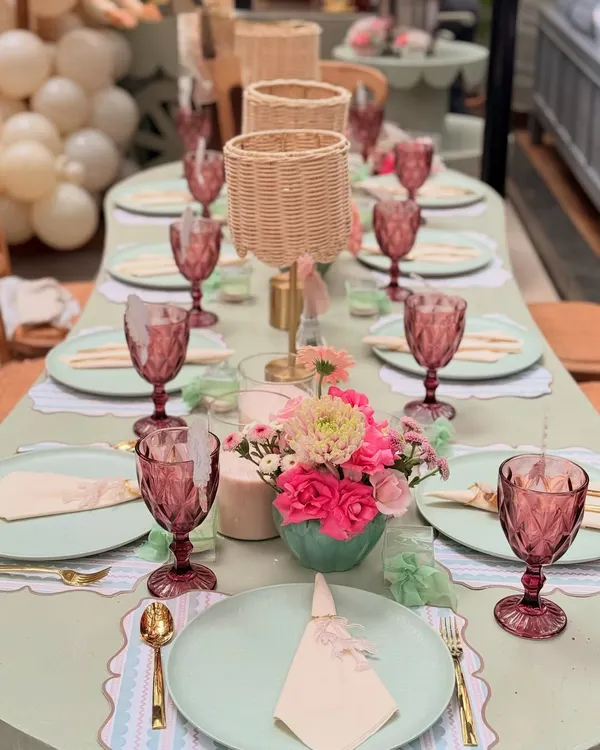 A top-down view of the Parisian baby shower tablescape, showing the harmony between the sage green plates, pink floral arrangements, and gold cutlery.