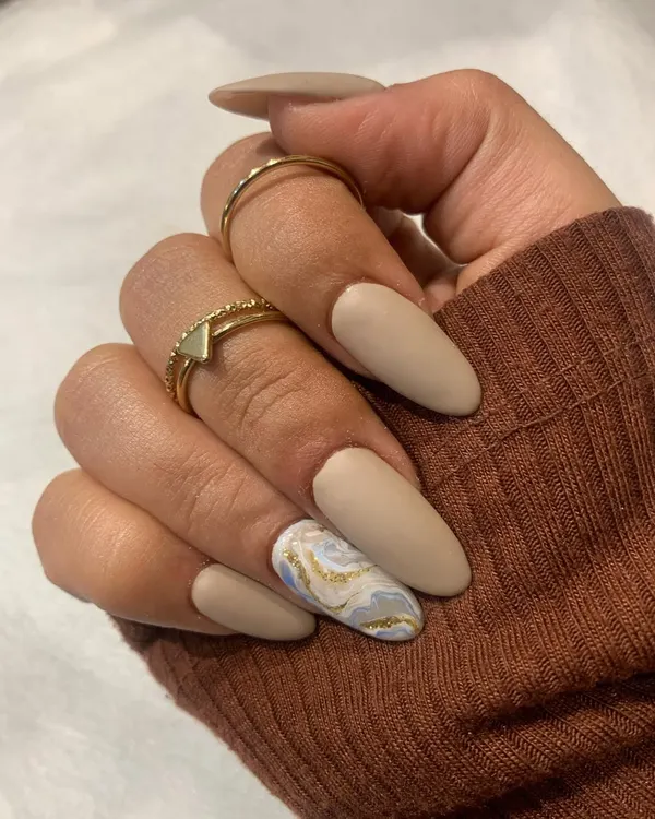 A beautiful matte finish manicure. This set features nude matte nails with a stunning marble accent nail in shades of white, grey, and gold.