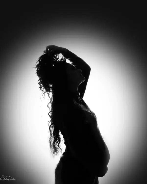 A stunning silhouette portrait of a mother to be. The backlighting creates a beautiful halo effect, highlighting her form and capturing a moment of quiet strength and beauty.