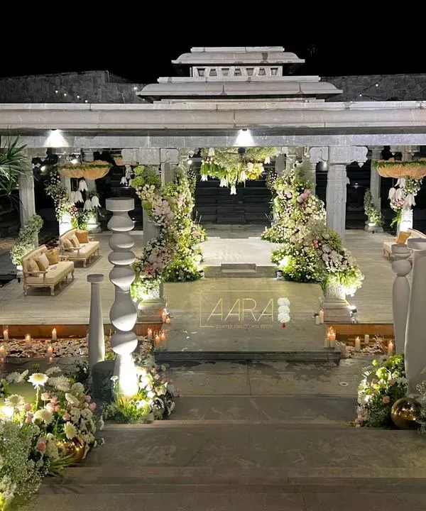 For a modern white wedding at Amita Rasa, I designed this stunning mandap within a stone pavilion. The structure was adorned with cascading white and pink florals, and the aisle was lined with candles, creating a magical ambiance as evening fell.