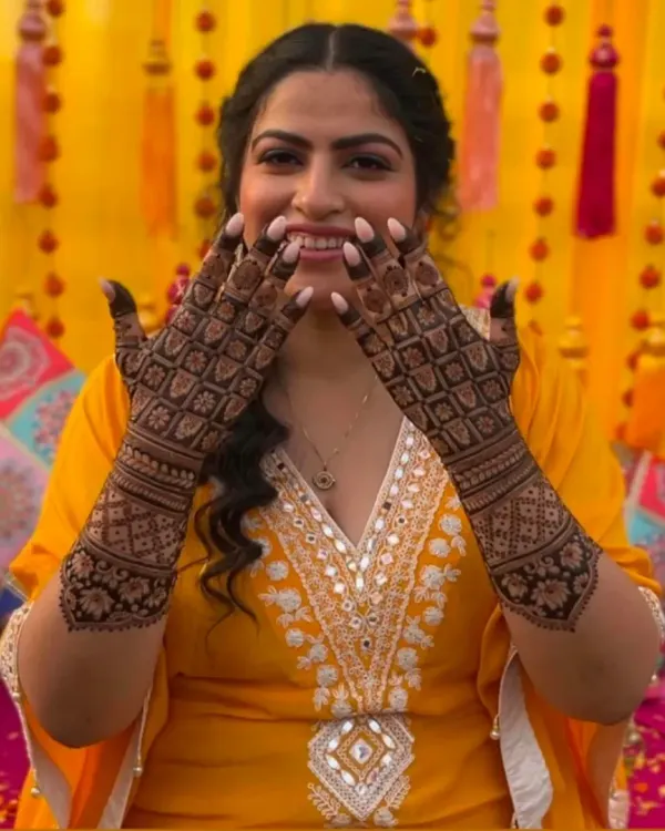A happy client showing her hands covered in a dense, geometric jaal pattern. This full-coverage mehandi is perfect for a bride or for major celebrations.