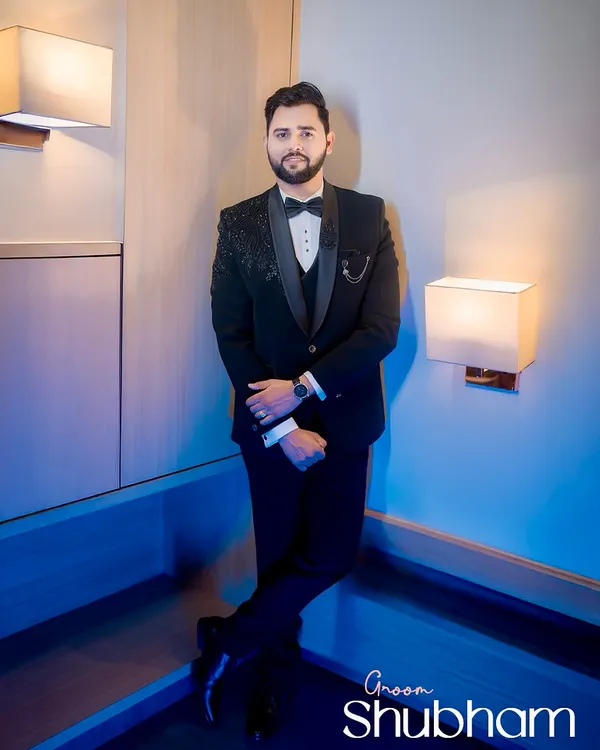 A full-length portrait of the groom, Shubham, looking sharp in his black tuxedo. The cool, blue-toned lighting adds a modern and sophisticated touch.