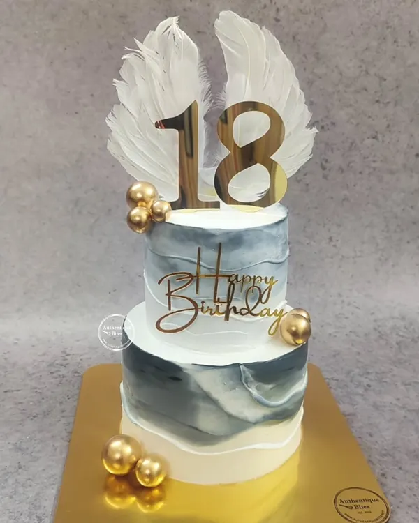 An angelic two-tiered cake for an 18th birthday. The design features a marble effect in grey and white, accented with gold spheres and topped with beautiful white angel wings.
