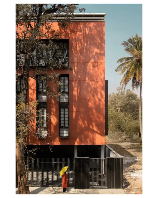 The building's east-facing orientation allowed us to strategically design openings that optimize natural light while minimizing heat gain. The monolithic red volume stands in striking contrast to the surrounding greenery.
