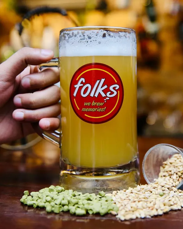 A classic shot for Folks brewpub. The branded mug is front and center, with raw ingredients like hops and barley scattered around to emphasize the 'craft' nature of the beer.