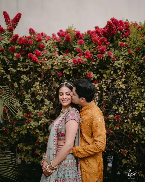 A sweet, candid moment between the couple at their Mehendi in Jaipur. The bride's makeup is fresh and radiant, with a soft pink lip that complements the floral embroidery on her Anita Dongre lehenga.