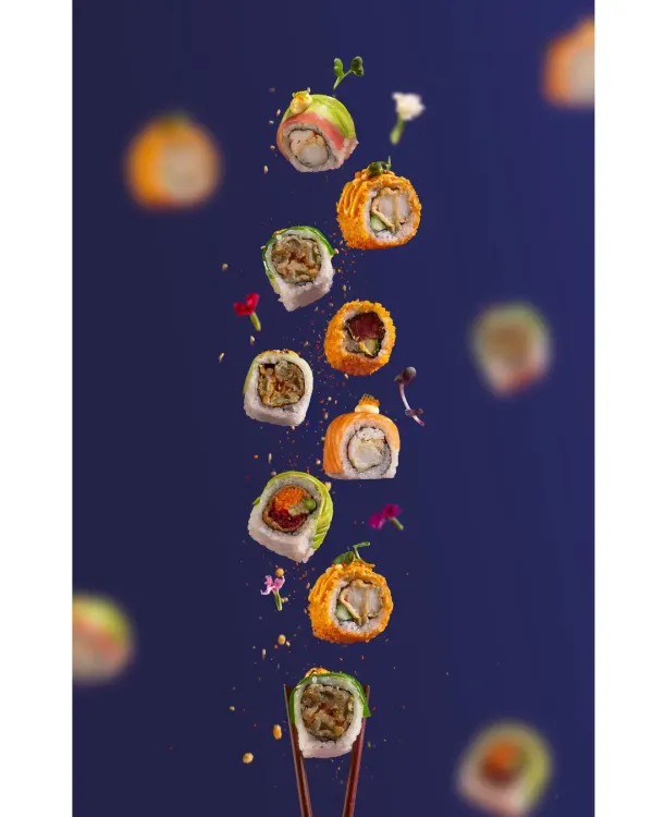 A creative levitating shot of assorted sushi rolls against a bold blue background, demonstrating advanced food styling and dynamic composition for Harajuku Tokyo Cafe.
