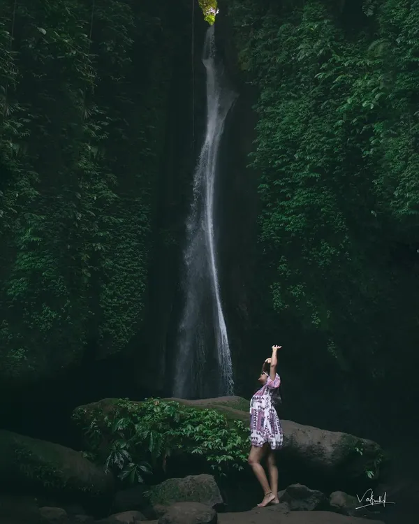 Chasing waterfalls and adventures in Bali. This wide shot captures the immense scale and beauty of the Leke Leke waterfall, with my wife standing in awe of the magnificent natural surroundings.