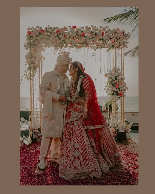 A picture-perfect moment from a Goa beach wedding. The floral arch, the sea in the background, and the happy couple create a stunning frame that perfectly captures the dream of a destination wedding.