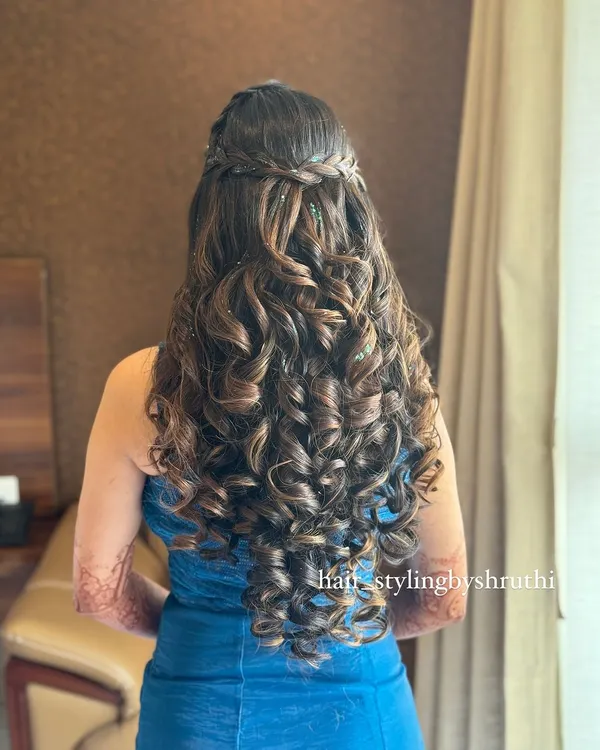 A half-up hairstyle with a crown braid and a cascade of tight, defined curls. This look is perfect for adding texture and volume, suitable for a sangeet or reception.