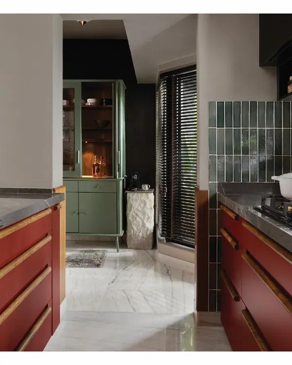 The kitchen is my solace. This is our personal kitchen, featuring Marsala red cabinetry with custom wooden handles. A standalone sage green bar cabinet and a stone pedestal for the coffee machine create a functional "Cook and Drink" unit, making the space both vibrant and highly practical.