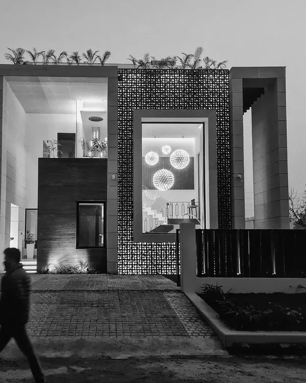 A dramatic black and white evening view of our "House of Frames" project, emphasizing its strong geometric volumes and the interplay of light. The design uses large openings and a perforated screen to create layers of transparency and privacy.