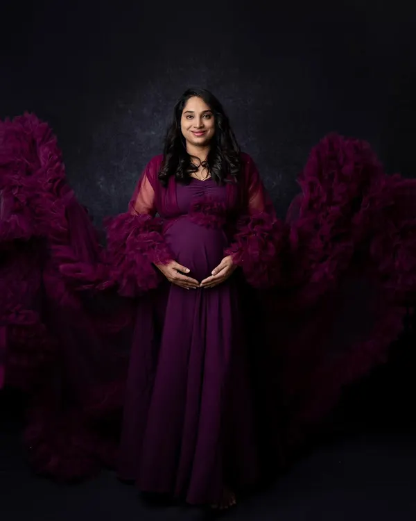 The full effect of this magnificent purple maternity gown, with its ruffled train spread out to create a sense of drama and elegance. This is a perfect example of a show-stopping studio maternity shot.