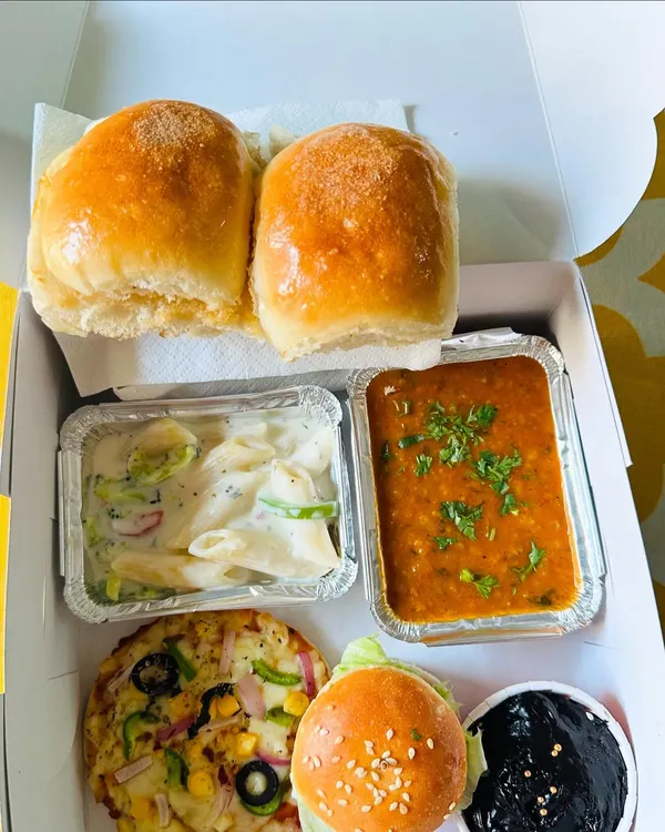 This is what I mean by a complete meal in a box. Here you can see a mini veg pizza, creamy white sauce pasta, classic pav bhaji, a mini burger, and a rich chocolate brownie, all packed fresh for a client's get-together.