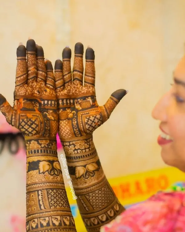 A lovely candid moment of a bride admiring her intricate mehendi. The design features traditional elements like peacocks, lotuses, and elephants.
