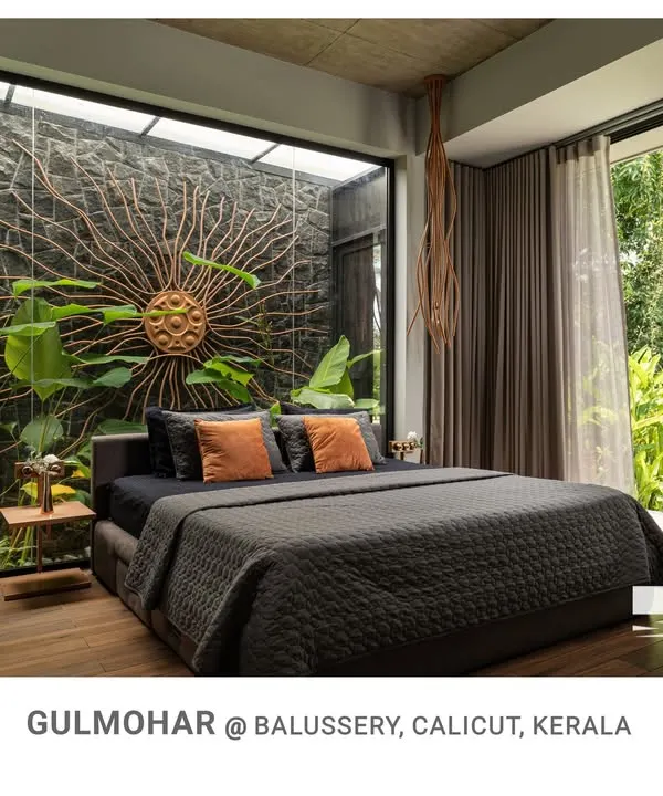 The master bedroom at Gulmohar is a true retreat, with a full-length glass wall opening to a private courtyard and a stunning sun-ray art piece on a natural stone wall.