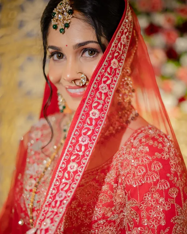 A captivating close-up of a bride in her red reception lehenga. The focus is on her sparkling eyes, enhanced with soft smoky makeup, and the delicate veil, creating a look of timeless royal beauty.