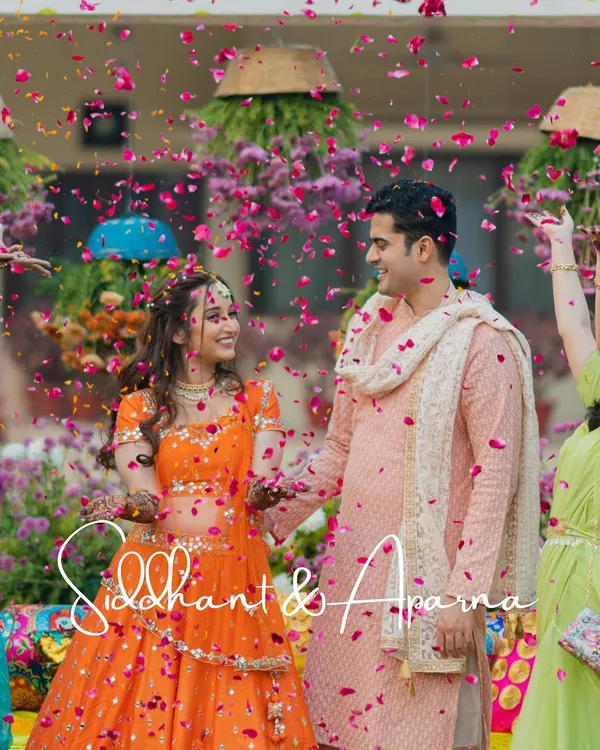 A beautiful shot of the couple under a shower of pink petals during their vibrant Mehendi ceremony.