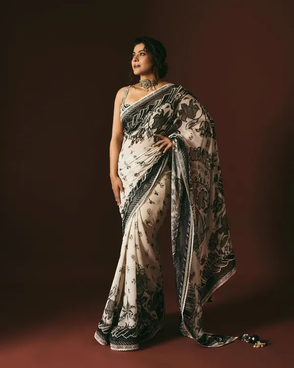 A full-length view of Kajol in a stunning black and white summer print saree. The look is paired with a statement choker, creating a style that feels like a piece of art from a gallery.