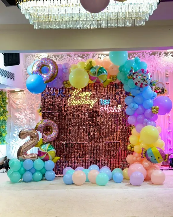 A vibrant candy-themed 2nd birthday party at a banquet hall. We used a colorful pastel balloon arch, a sparkling shimmer wall, and custom neon signs to create a magical atmosphere for the little one.