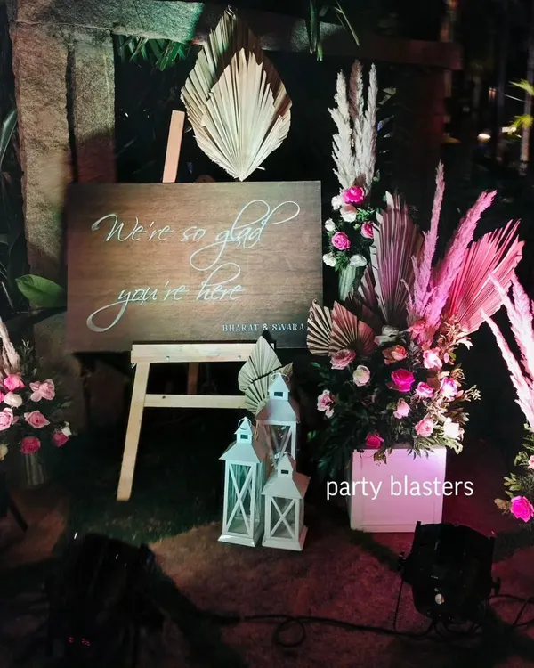 A warm welcome for your guests sets the tone for the event. This rustic wooden sign is paired with bohemian-style dried palms, fresh pink roses, and lanterns to create a chic and inviting entrance.