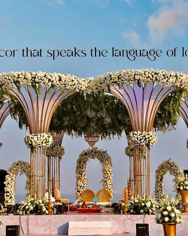 This grand mandap, set against the open sky, is one of my signature destination wedding designs. The structure features large, trumpet-like pillars topped with dense white chrysanthemums and filled with lush greenery, creating a breathtaking focal point for the ceremony.