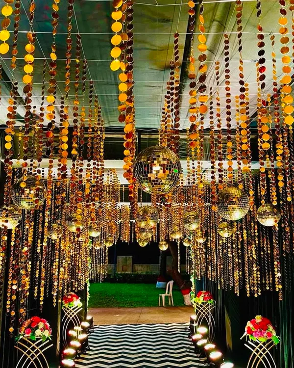 A dazzling entrance tunnel designed for a Sangeet night. The ceiling is covered with hanging strings of golden sequins and multiple disco balls, creating a shimmering, immersive experience for guests as they walk in.