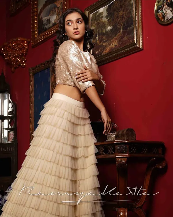 A glamorous ensemble perfect for a cocktail party or sangeet. The shimmering beige sequin crop top is paired with a multi-layered tulle frilled lehenga for a dramatic and modern look.