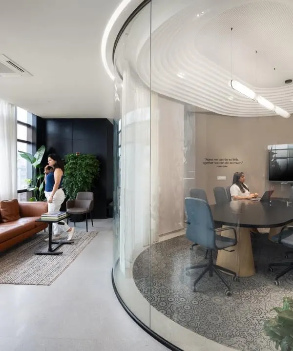 A glimpse into a modern workspace we designed, featuring a curved glass conference room for transparent collaboration, alongside a comfortable lounge area with stunning city views. This project highlights our approach to blending formal meeting areas with informal breakout zones.