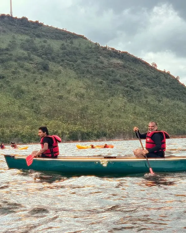 Participants enjoy a peaceful canoeing session on the waters of Vani Vilas Sagar, with the green hills providing a beautiful backdrop.