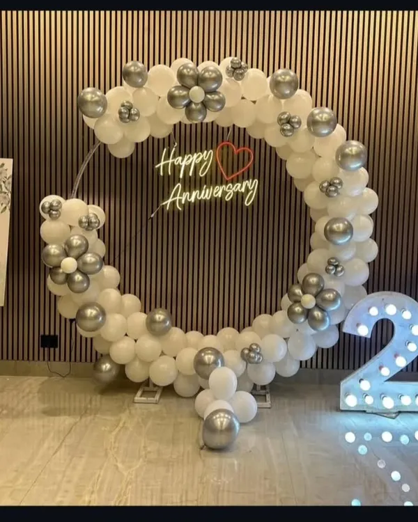 An elegant setup for a 25th wedding anniversary. The large circular balloon arch in white and silver, a custom neon sign, and big light-up "25" numbers create a sophisticated photo backdrop.
